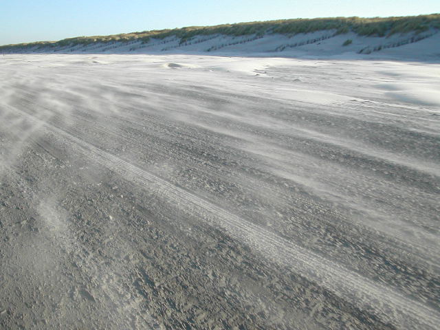 Zand stuift over het strand